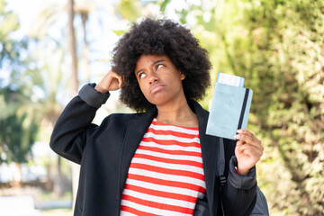 African American girl holding a passport at outdoors having doubts and with confuse face expression