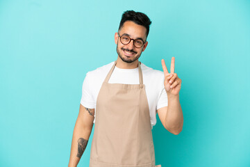 Restaurant waiter caucasian man isolated on blue background smiling and showing victory sign