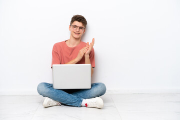 Teenager Russian man holding pc sitting on the floor isolated on white background applauding after presentation in a conference