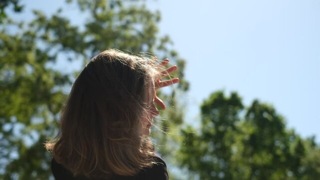 portrait of a young woman squinting and covering her face with her hands from the bright sun in a park on a summer day