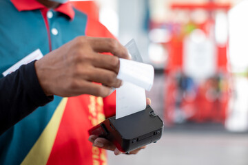 Hand of cashier pull slip from credit card reader with blurry gas station background.  Buy and sell products & service. The concept of payment in gas station.