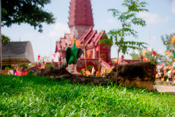 A low-angle shot of a green lawn with a blurry brown Khmer temple in the background , Wat Luang Pu Suang.Wat Phrai Phatthana