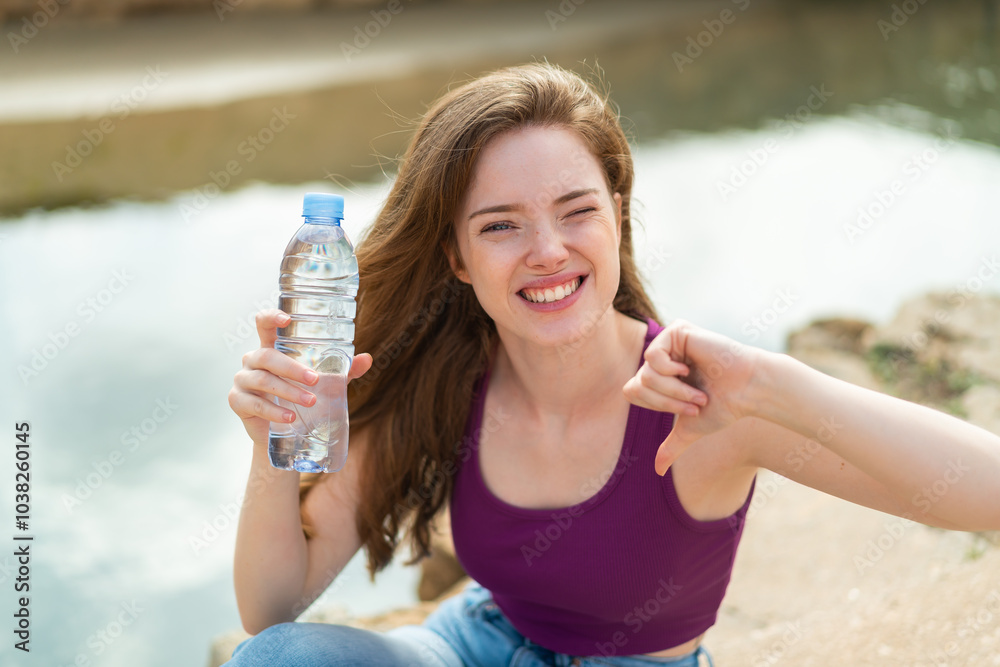 Poster Young redhead woman with a bottle of water at outdoors proud and self-satisfied