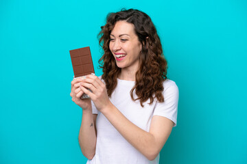 Young caucasian woman isolated on blue background taking a chocolate tablet and happy