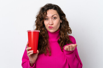 Young caucasian woman drinking soda isolated on white background making doubts gesture while lifting the shoulders
