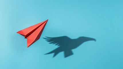A vibrant red paper airplane casting a shadow of a bird on a blue background, symbolizing freedom and creativity.