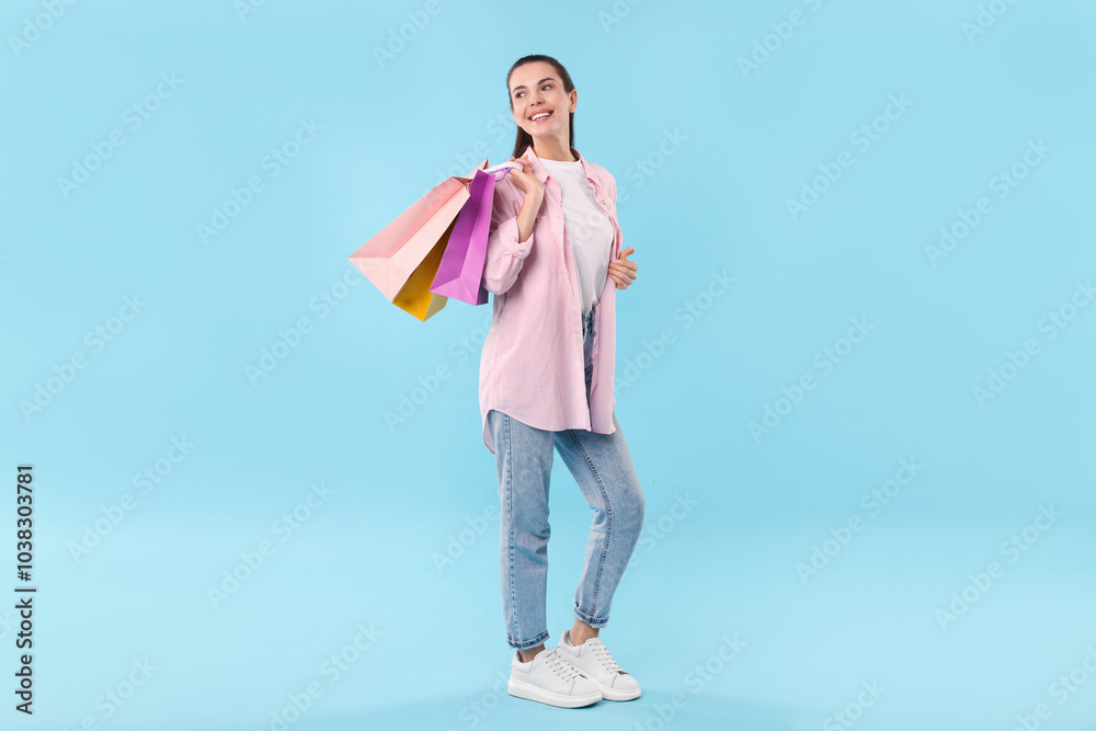 Wall mural smiling woman with colorful shopping bags on light blue background