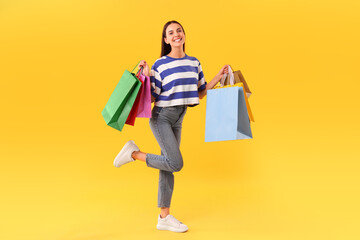 Smiling woman with colorful shopping bags on yellow background