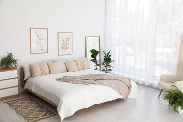 Large bed, houseplant and full-length mirror near window in room. Stylish bedroom interior