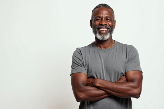 Smiling middle aged black man with beard and graying hair arms crossed in gray t shirt on white background
