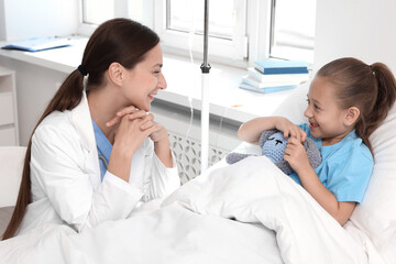 Doctor examining little girl on bed at hospital