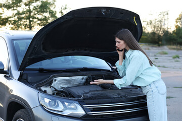 Stressed woman talking on phone near broken car outdoors