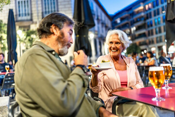 Senior man eating tapas next to partner in sidewalk cafeteria