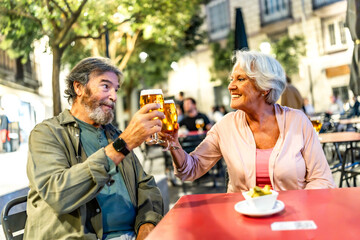 Senior couple toasting with beer in sidewalk cafeteria at night