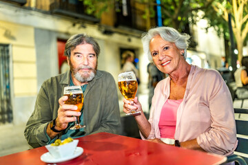Senior couple toasting at camera with beer in outdoor terrace