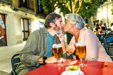Senior couple kissing while drinking beer in an outdoor terrace