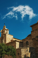 Fototapeta premium Old spanish church with tree in sunlight under blue sky with clouds.
