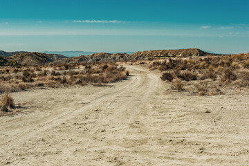 Dirt road in arid mountainous landscape on a sunny day with blue sky.