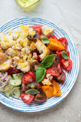 Middle close-up of panzanella or italian tomato and bread salad, vertical shot on a beige stone background, elevated view