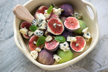 Beige serving tray with sliced figs, blue cheese and green basil, horizontal shot on a grey granite surface, middle close-up
