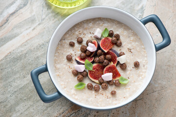 Breakfast oatmeal with figs, chocolate balls and marshmallow, horizontal shot on a grey and roseate granite surface, elevated view