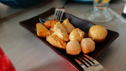 Delicious Assorted Fish Balls, Shrimp Balls, Kekian, Batagor, Pempek, Dimsum, Fried Dumplings on Black Square Plate, Popular Asian Street Food Platter, Restaurant Style, Blur Background Presentation
