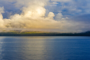 Morning clouds over land of pine trees and ocean water near Juneau, Alaska