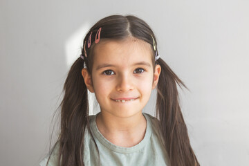 close-up portrait of a 6 year old brunette girl with two ponytails, looking at camera, showing one front tooth that has fallen out
