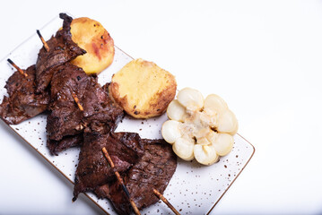 Grilled Peruvian anticuchos with potato and corn sides.