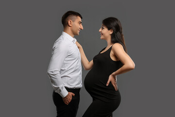 Beautiful pregnant woman with her husband on grey background