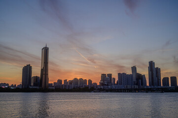 Obraz premium Sunset and silhouette view of 63 Building and high rise buildings of financial district with Wonhyo Bridge on Han River at Yeouido near Yeongdeungpo-gu, Seoul, South Korea