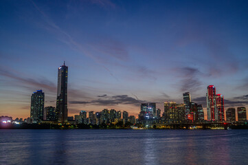 Obraz premium Sunset and silhouette view of 63 Building and high rise buildings of financial district with Wonhyo Bridge on Han River at Yeouido near Yeongdeungpo-gu, Seoul, South Korea