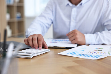 Banker using calculator at wooden table in office, closeup