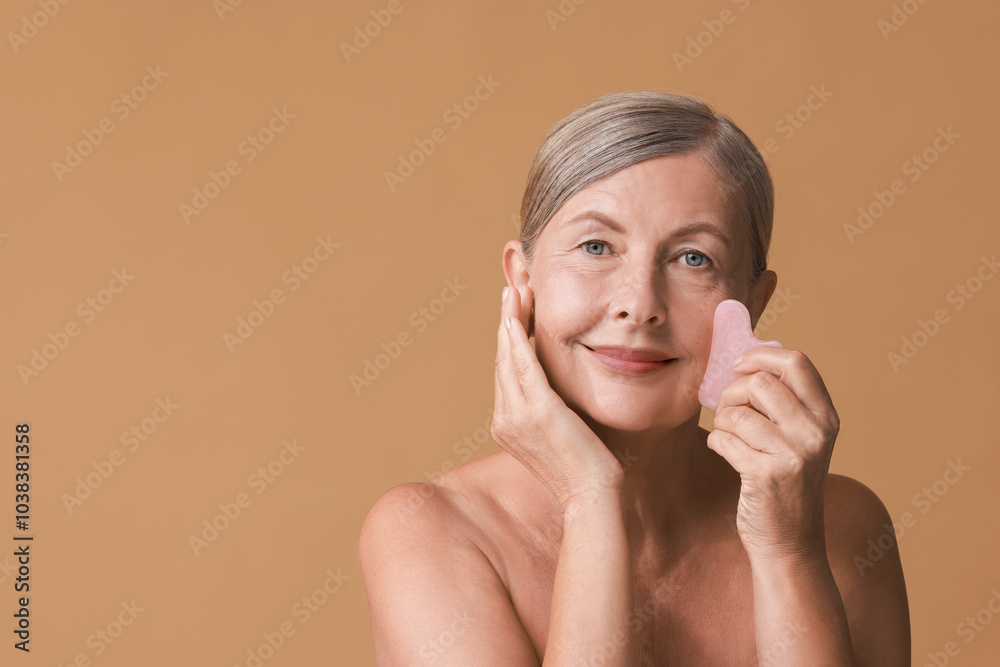 Wall mural Beautiful woman doing facial massage with gua sha tool on beige background, space for text