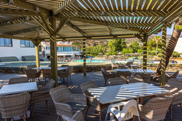 Wicker chairs and tables on outdoor terrace under pergola near swimming pool with mountain view. Crete. Greece. 