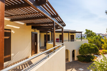Fototapeta premium Shaded corridor hotel with wooden beams, doors, and bright sunlight casting shadows. Crete. Greece.
