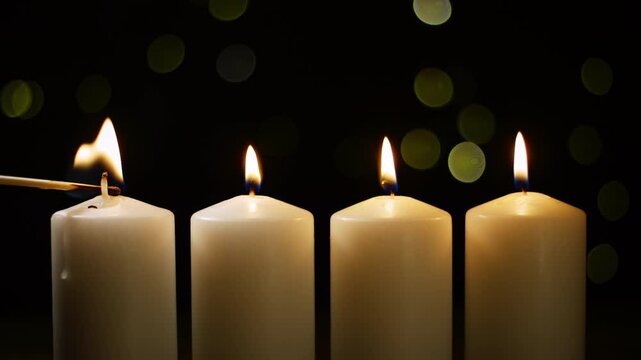 Hand lighting a fourth white Advent candle with a safety match, festive bokeh lights in a background, close up shot. Winter holidays concept.