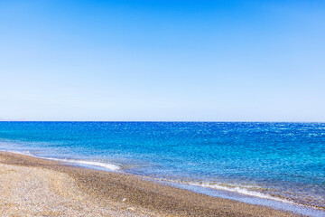 Calm Mediterranean Sea with pebble beach on Crete island, Greece, under clear blue sky.