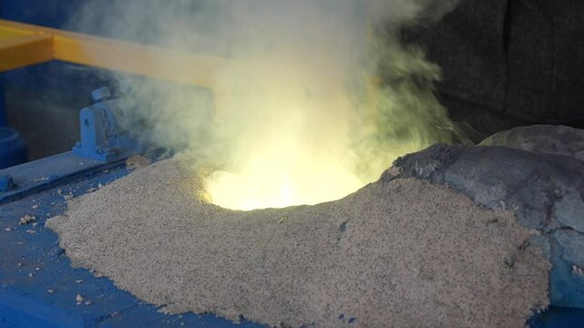 Iron casting in smelter factory. Foundry worker pouring liquid steel into molds. Worker in foundry pouring hot metal into mold. Molten iron casting production and metallurgy.