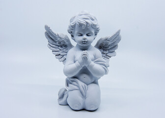 A white angel statue kneels and prays with eyes closed