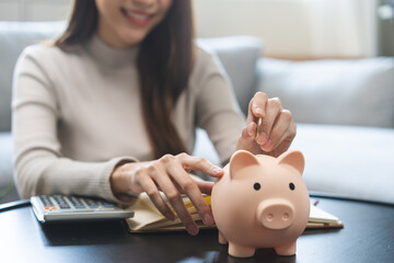 Saving money wealth concept, asian young business woman hand putting coin into piggy for saving...