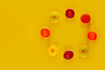Circle of round jelly candies lie on yellow background. Sugary circles on colorful backdrop
