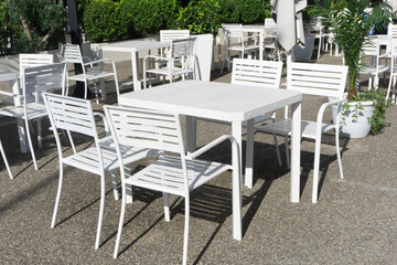 Outdoor beer garden. Drinking coffee in the sun at a park café. Restaurant seating area in a natural, open-air setting. Relaxing at an outdoor café. White chair and tables background.