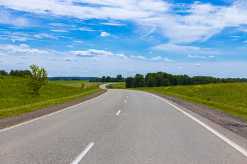 Winding curve of the Chuysky trakt road among summer green meadows under a blue sky in the Altai Republic, Russia. Russian route R256 or Chuya Highway at Altai.