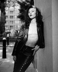 Monochrome image of confident rock star female leaning on wall.