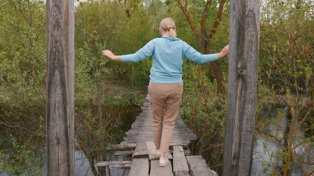 A woman, seen from behind, walks across a shaky suspension bridge over a river, overcoming her fear