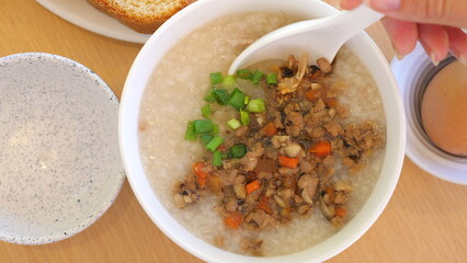 Close-up of congee with minced pork, green onions, carrots on wooden table. Comfort Food and Traditional Cuisine