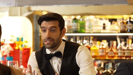 Good looking bartender warm smiling friendly conversation with couple customer at beverage bar counter while serving welcome drink with charm professionalism recommending special menu list. Vinosity.