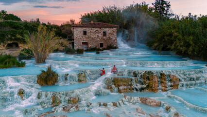 Bathe in the warm, turquoise waters of Saturnia thermal baths, surrounded by lush greenery and a serene sunset glow. Relax and rejuvenate amid nature's soothing beauty in Tuscany, Italy.