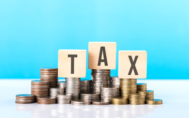 TAX is write on a wooden block next to a stack of coins. Against light blue background. Tax awareness, financial planning, savings, and effective money management